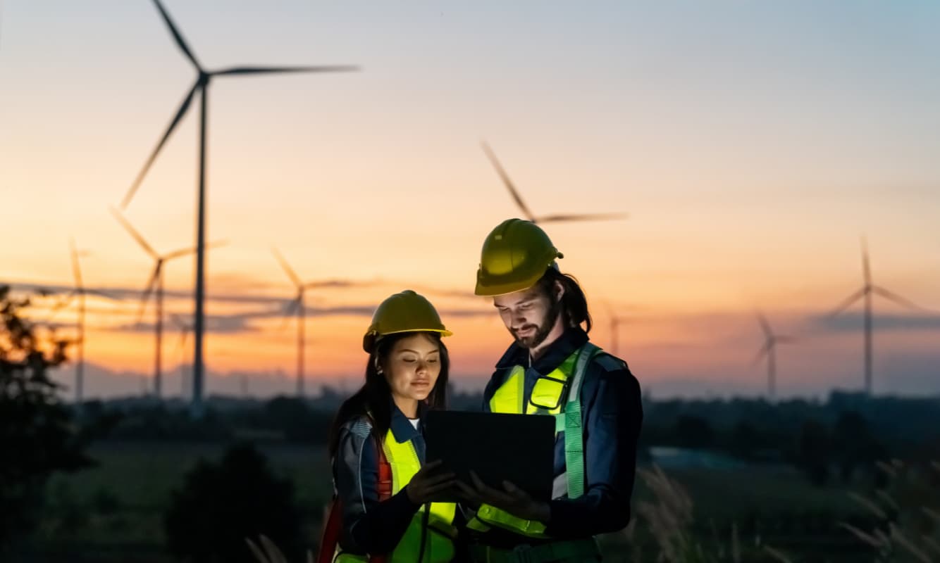 Workers in front of wind turbines helping to power eco-friendly manufacturing.